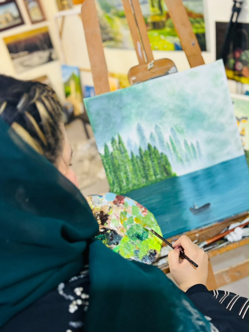Zuhra mixing colors while painting a mountain landscape